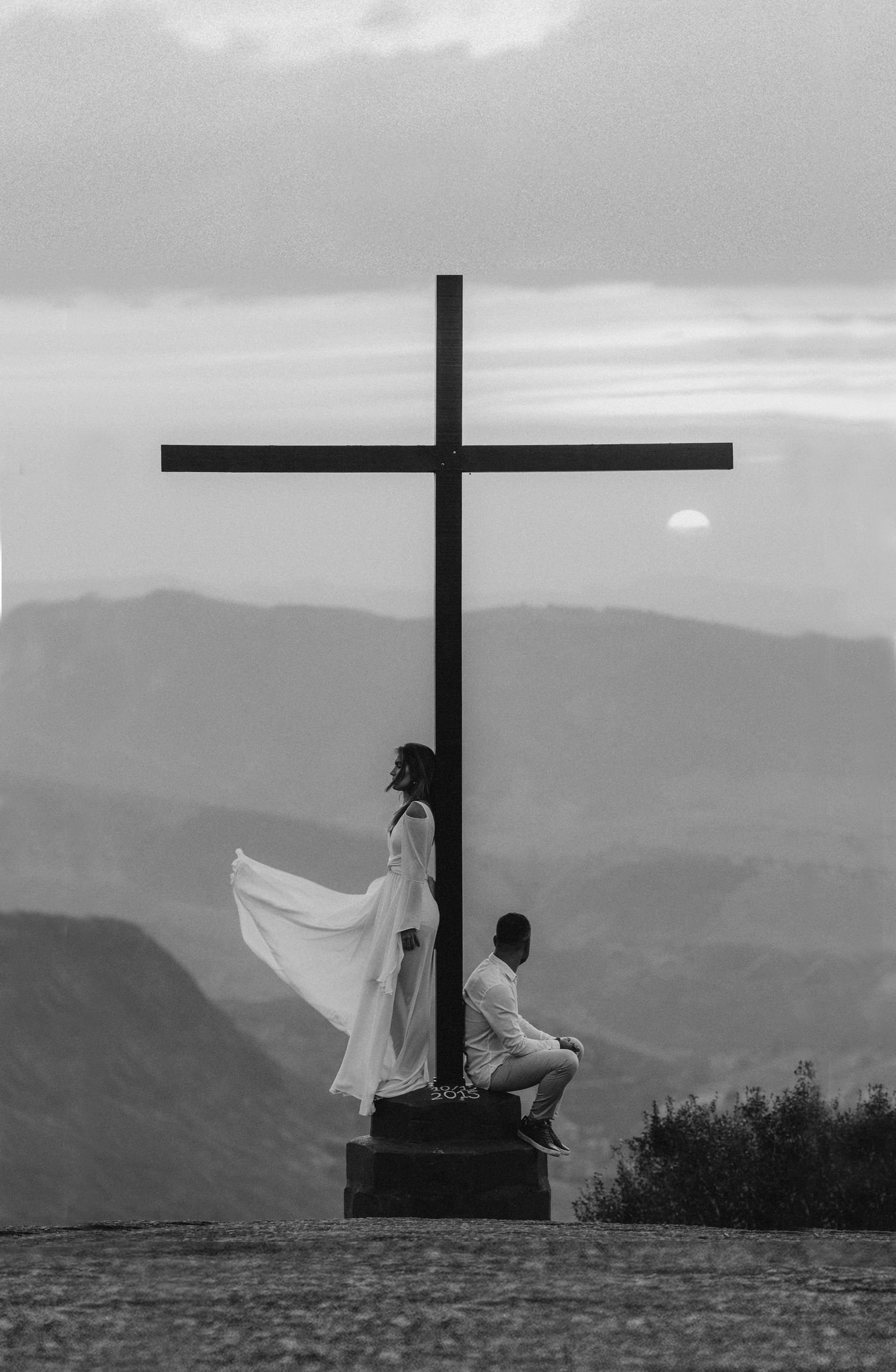 A serene moment of spiritual reflection by a cross at sunset with a dramatic sky in the background.