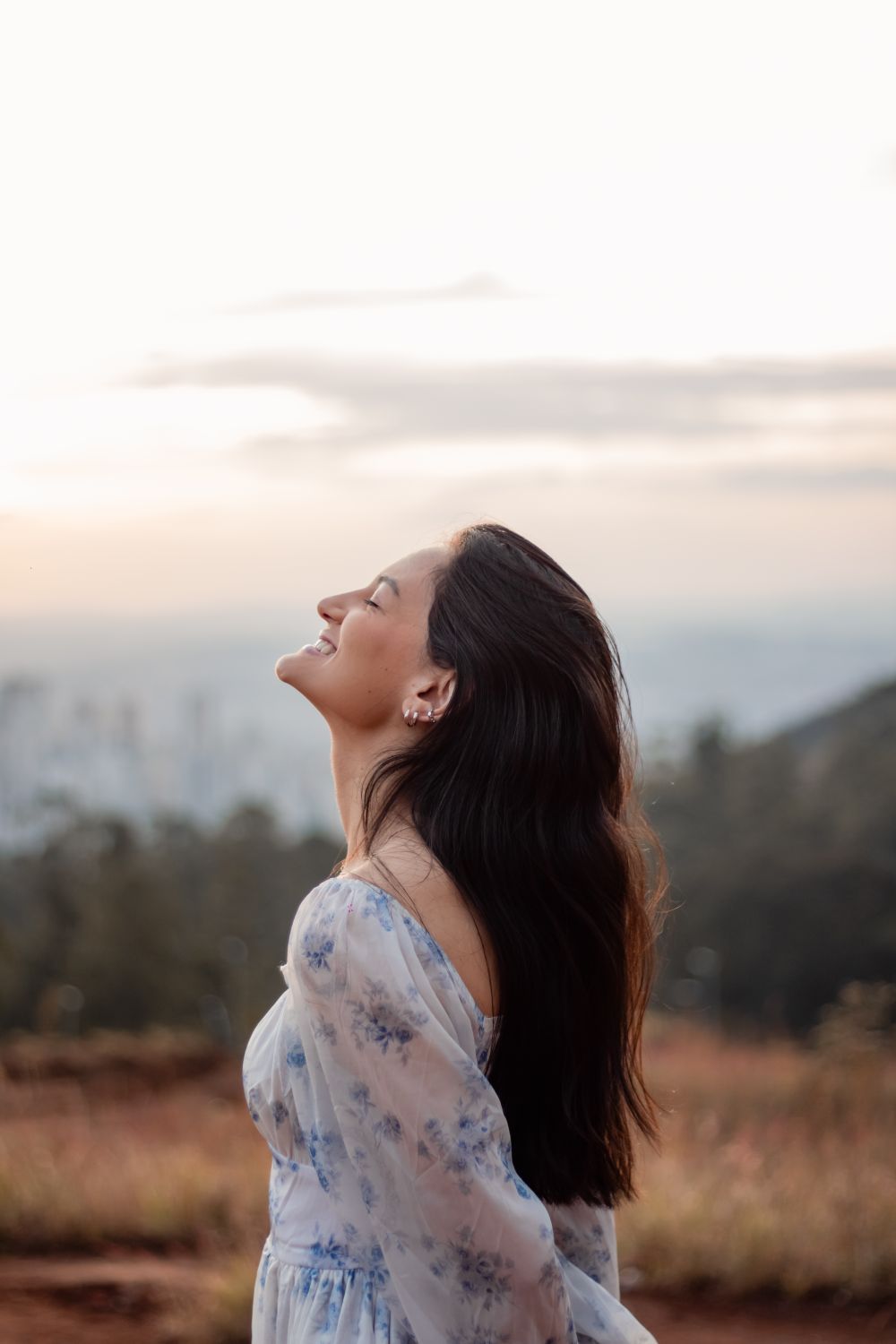 Serene outdoor portrait of a smiling woman enjoying the sunset in a peaceful landscape.