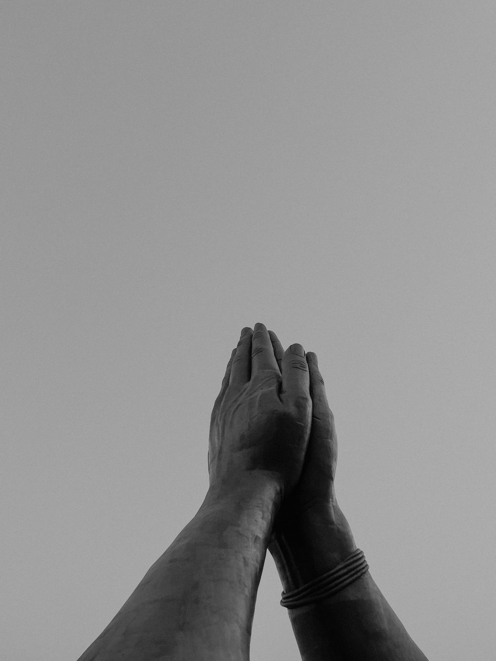 Monochrome image of hands in a prayer pose set against a clear sky, conveying meditation and spirituality.
