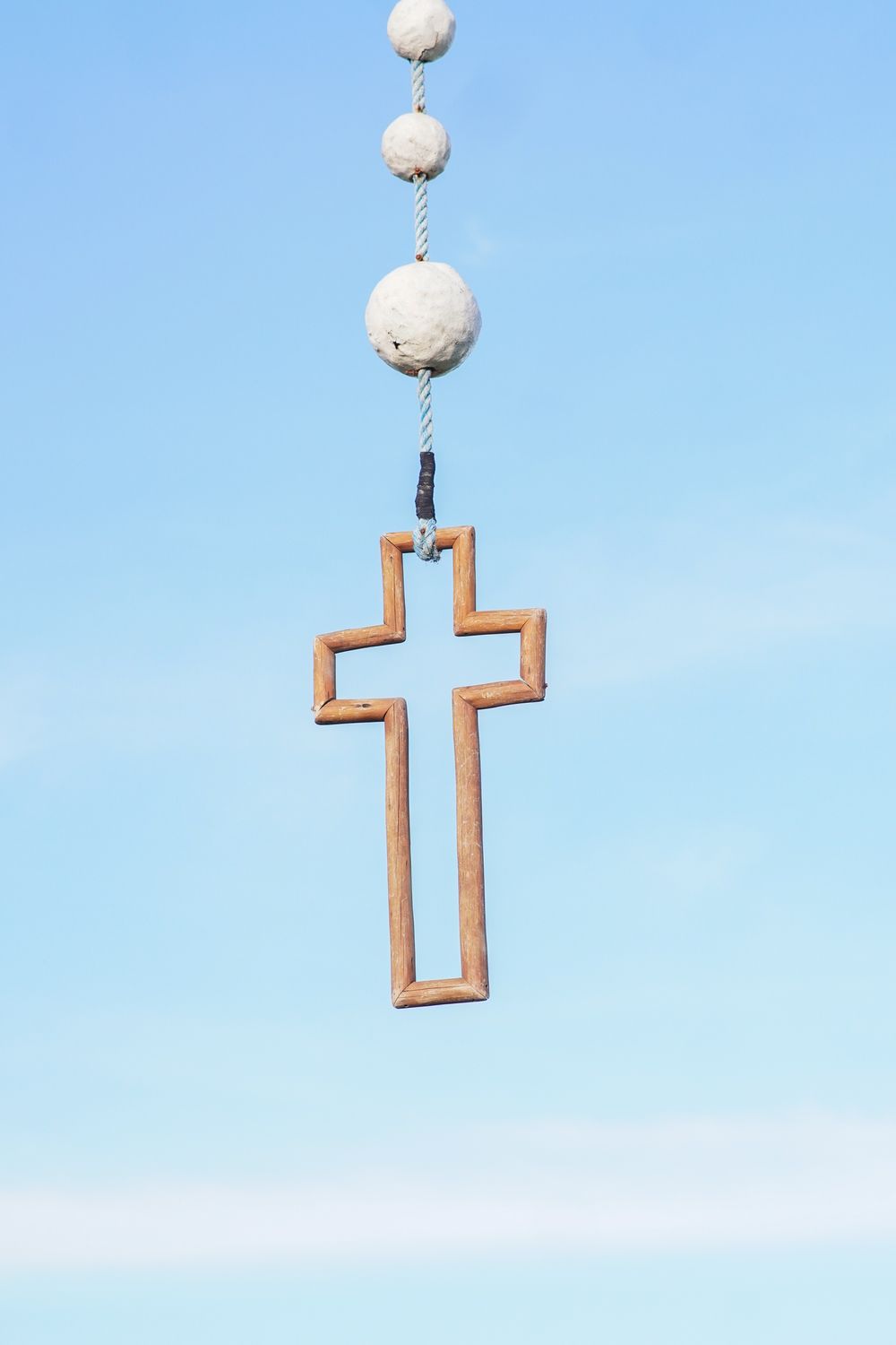 A minimalistic wooden cross pendant suspended in front of a bright blue sky.