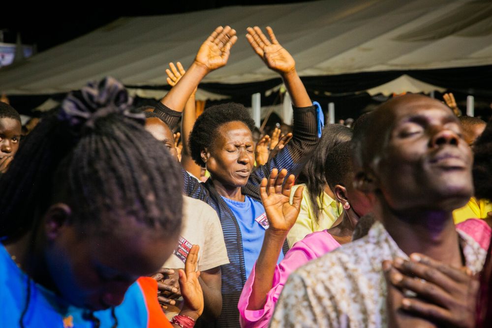 A joyful and diverse group of adults engage in a spirited prayer session outdoors at night.