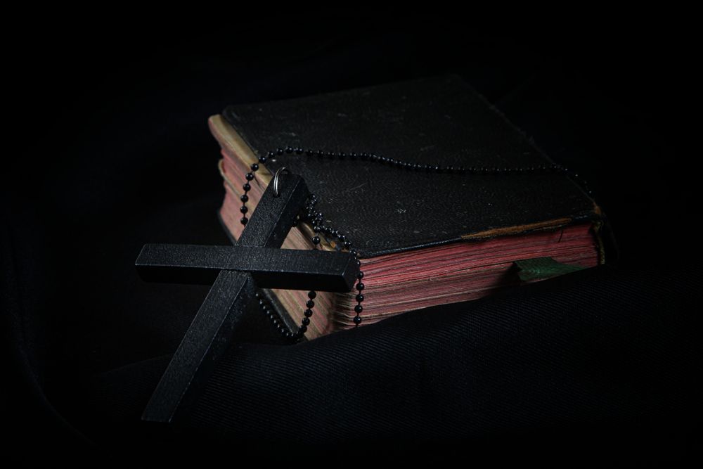 An old Bible with a black cross on a dark background, symbolizing faith and spirituality.