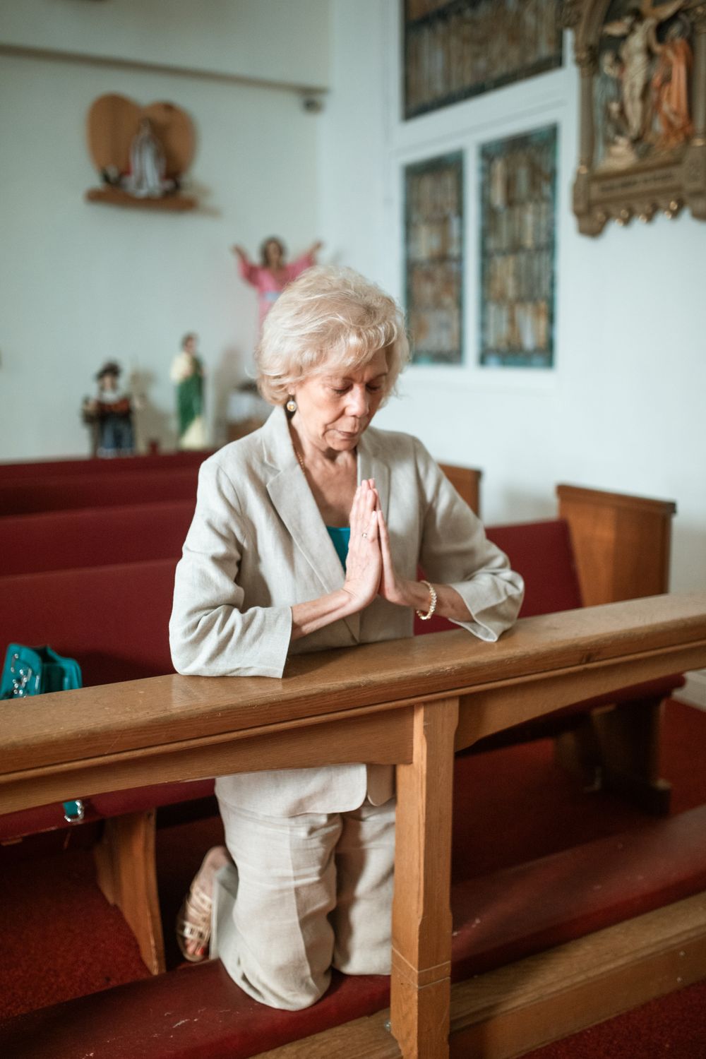 A devout senior woman kneels in prayer within a church setting, embodying faith and spirituality.
