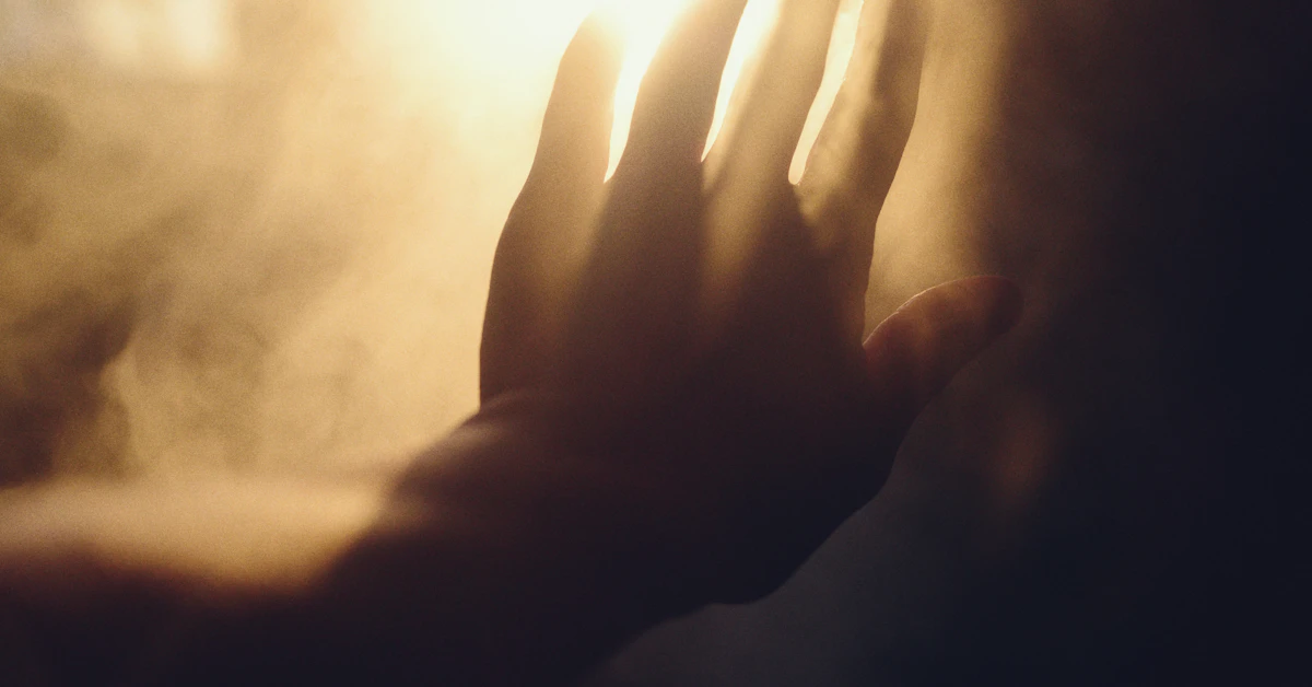 A hand reaching towards bright light through smoke