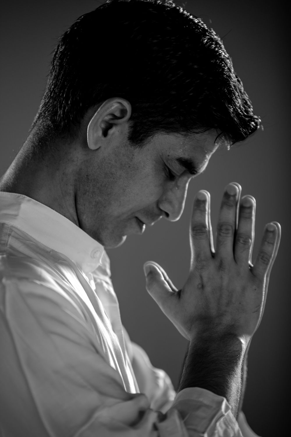 Side view black and white portrait of a man praying with eyes closed.