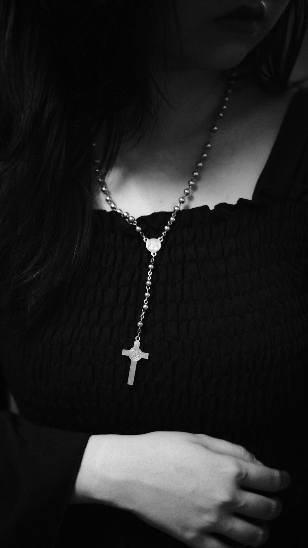 Black and white portrait of a woman wearing a rosary, evoking spirituality and reflection.