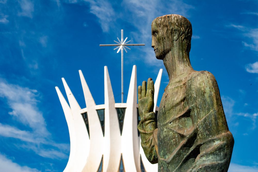 Close-up of a statue in front of the iconic Cathedral of Brasília under a clear blue sky.