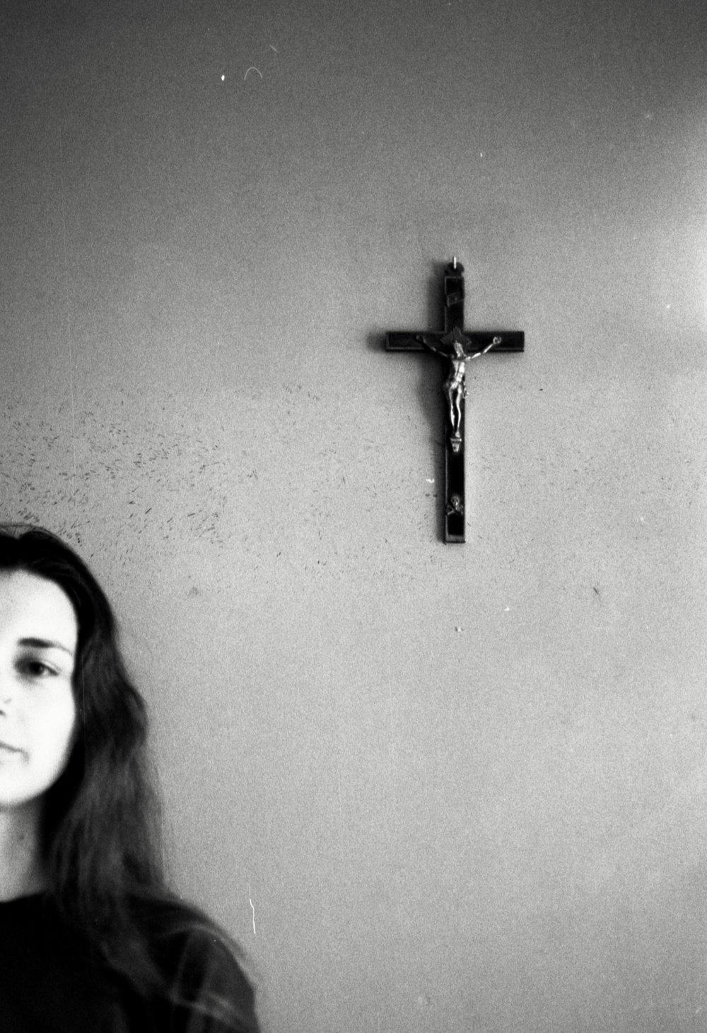 Atmospheric black and white photo featuring a crucifix and partial portrait of a woman in contemplative mood.