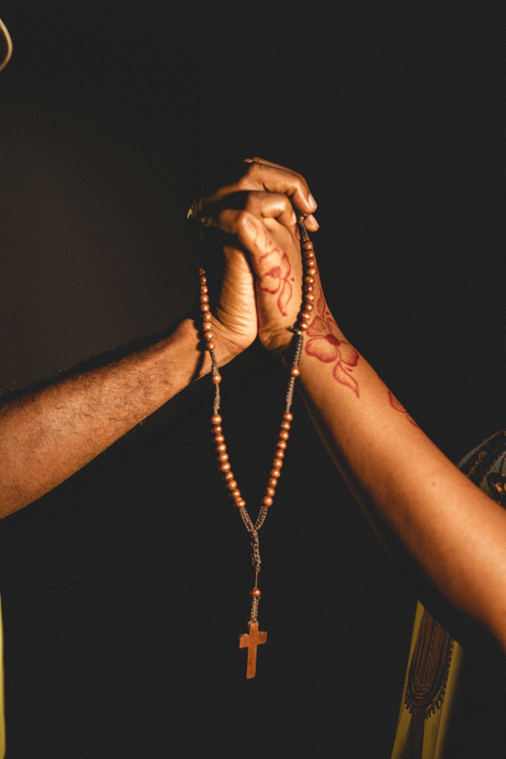 Two hands of diverse ethnicities clasping a rosary, symbolizing unity and faith.