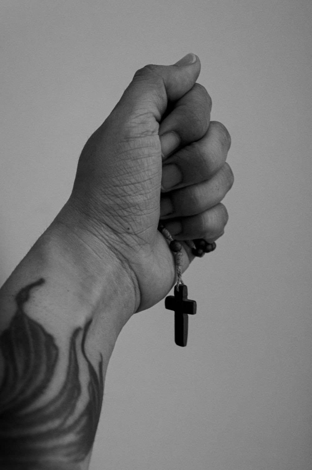 Close-up of a tattooed hand holding a cross pendant, evoking themes of faith and strength.