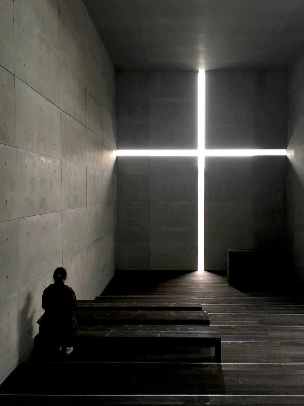 A lone person reflects in a modern church with a striking cross light feature.