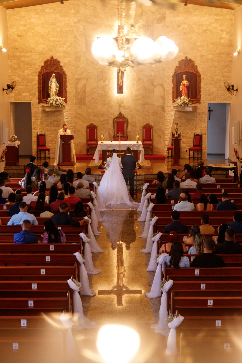An elegant wedding ceremony in a beautifully decorated church with attendees seated in pews.