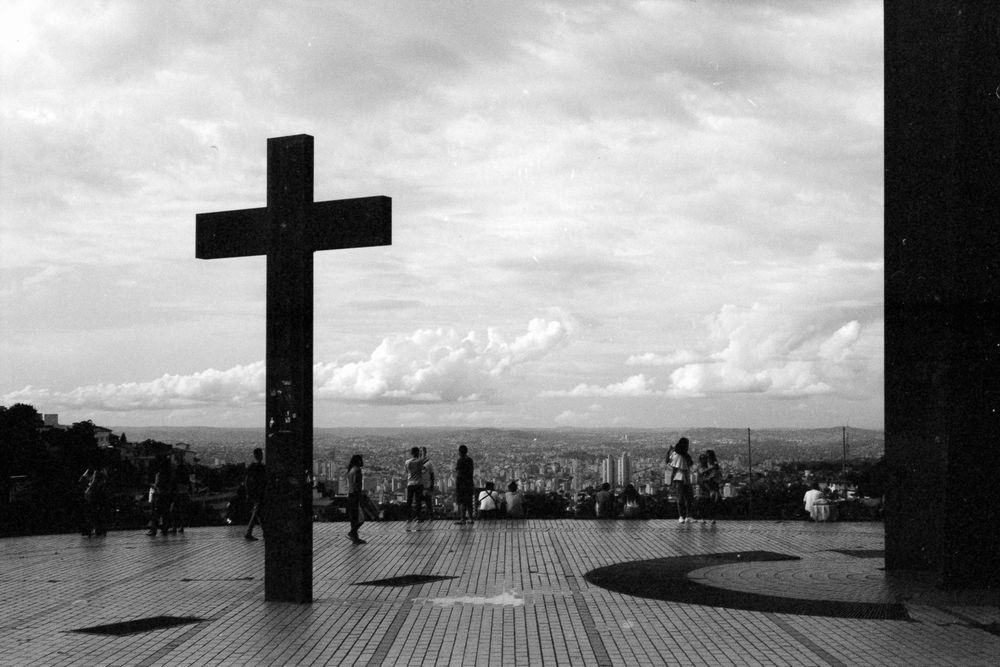 Black and white high viewpoint with sculpture of cross and people walking with cityscape on background