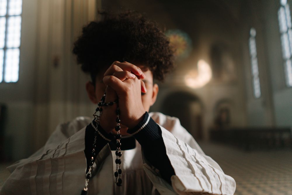Young boy praying with a rosary in a church, capturing devotion and faith.