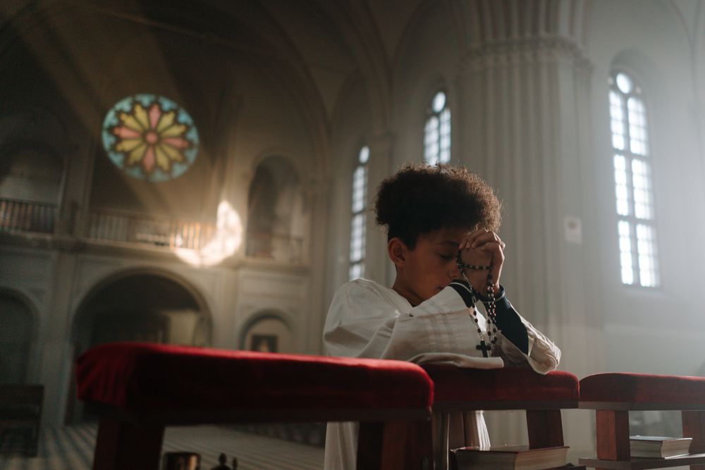 Child praying with rosary in a serene cathedral setting, sunlight through stained glass.