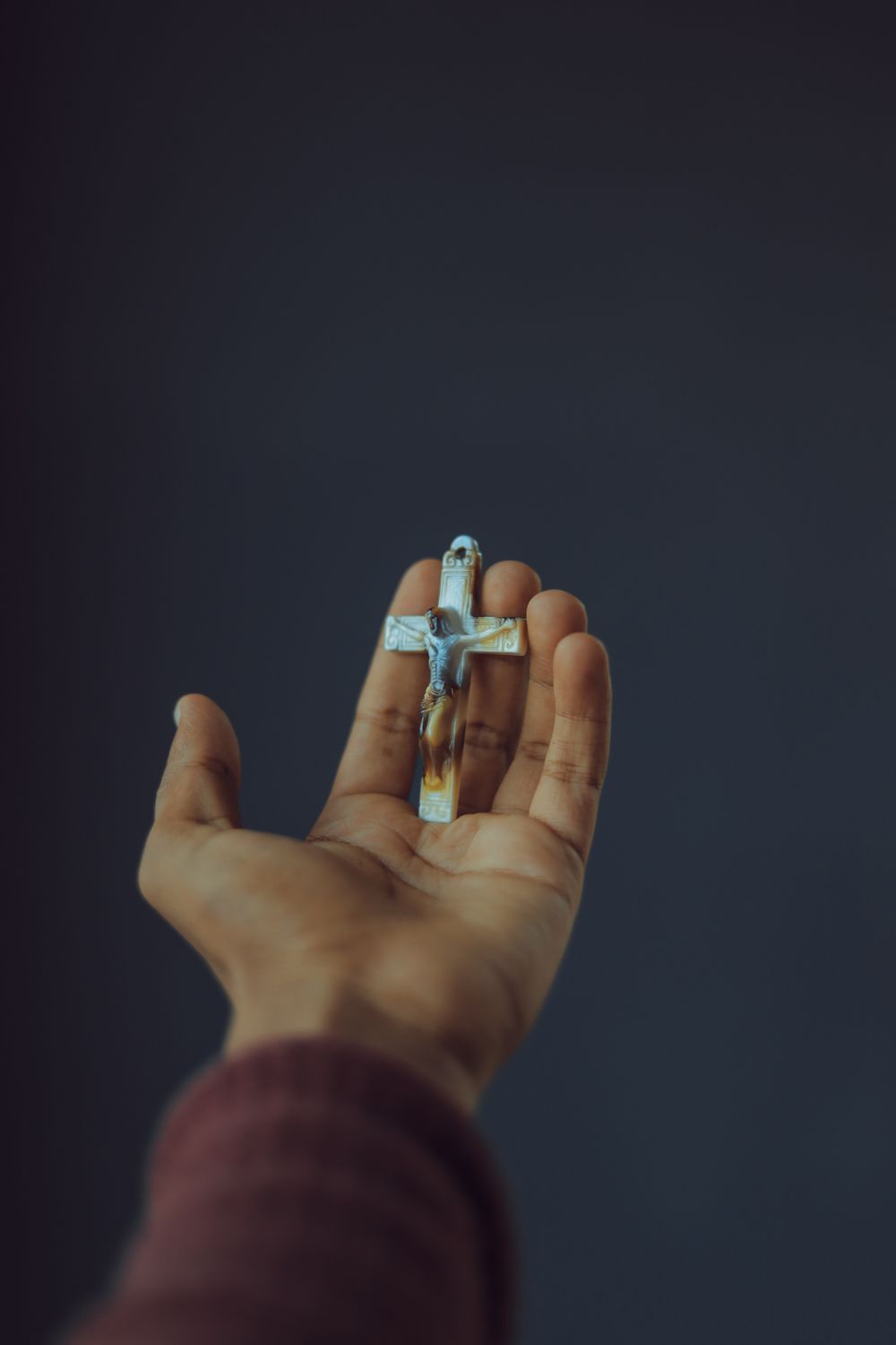 A contemplative image of a hand holding a crucifix against a gray background.
