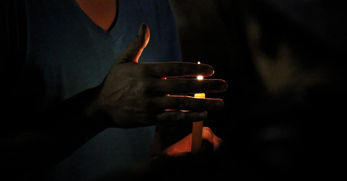 Hands holding a lit candle in darkness